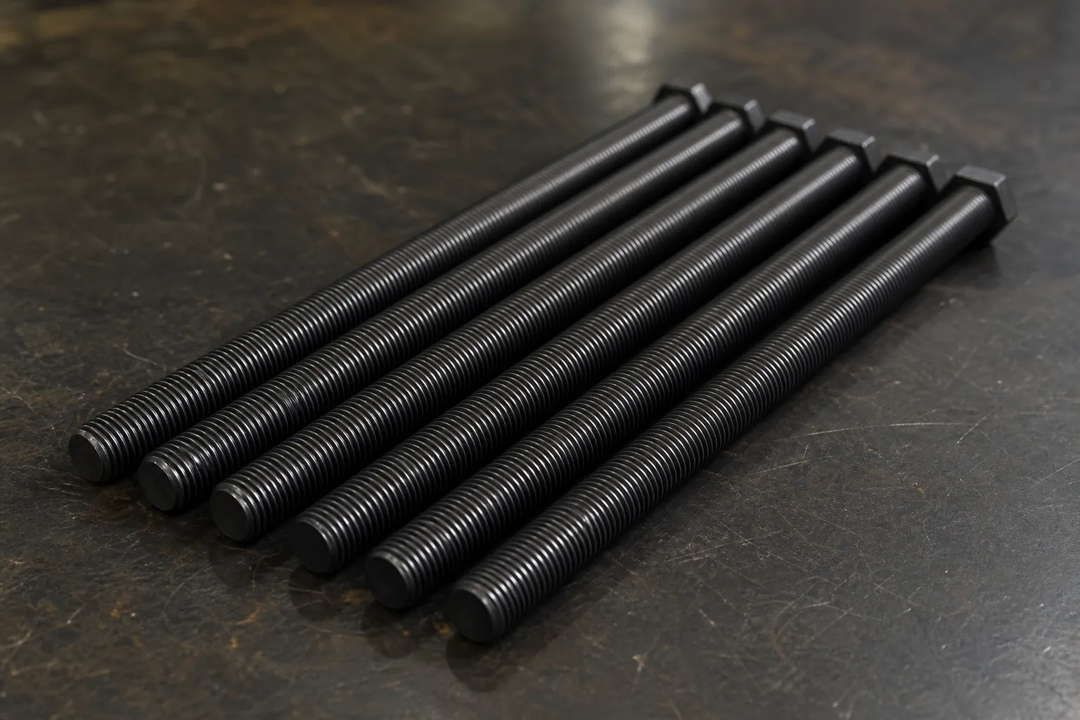 High-strength long bolts with rolled threads arranged on a dark workshop workbench, the typical workpiece for automated straightening